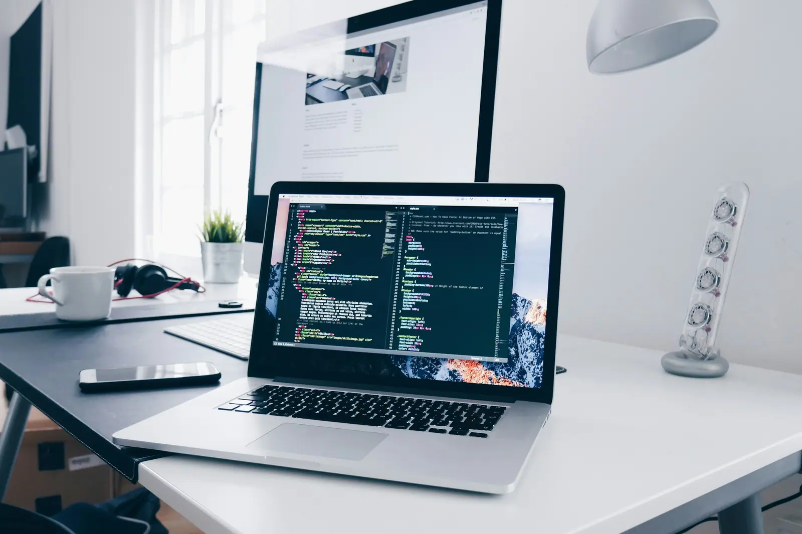 Laptop sobre un escritorio blanco mostrando código, junto a un teléfono y una taza