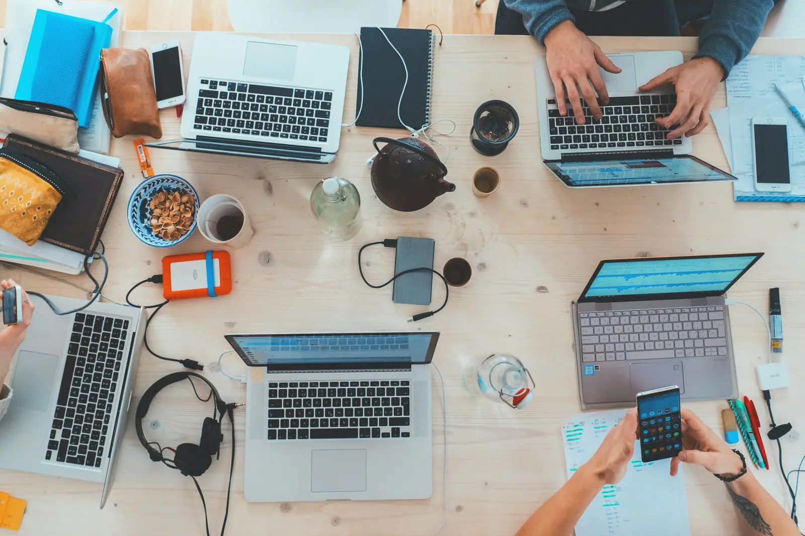Vista cenital de una mesa de trabajo compartida con laptops, teléfonos, auriculares y cuadernos